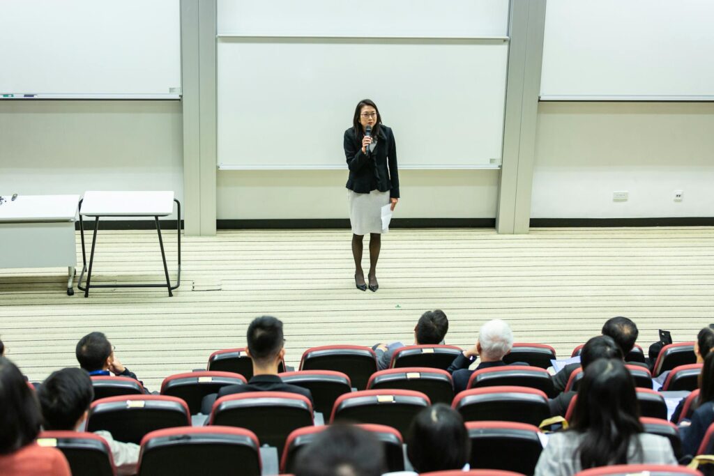 Woman with a microphone at the front of a lecture theatre teaching to students, in higher education.