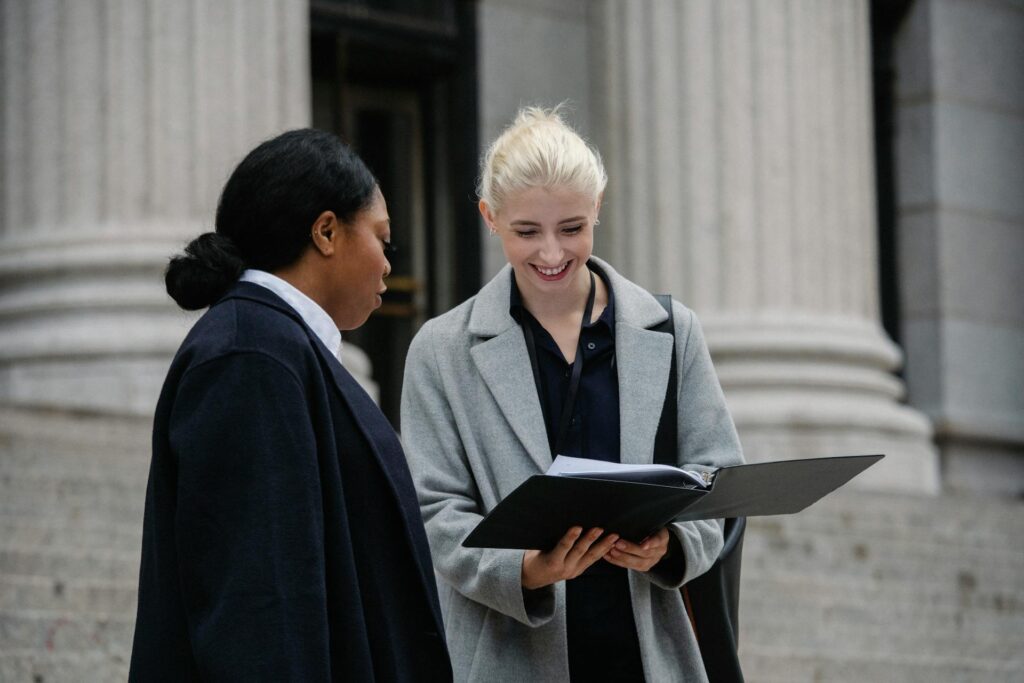 Two university leaders looking at information in a binder together outside a building with white roman pillars.